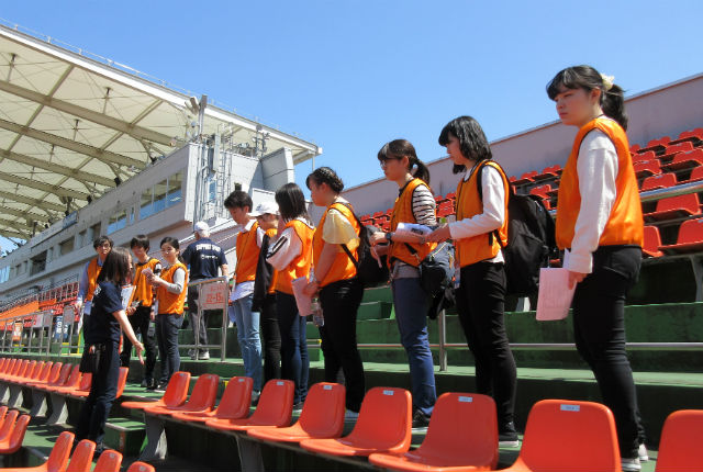 子ども学科の学生と地域社会学科の学生たちは明治安田生命J2リーグの大宮アルディージャの試合でボランティア活動を行い、ボランティアスタッフからボランティアの内容やスタアジアムの説明を受けました。